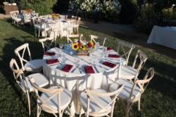 Elegant outdoor wedding setup with round tables, white tablecloths, and floral centerpieces on a sunny day.